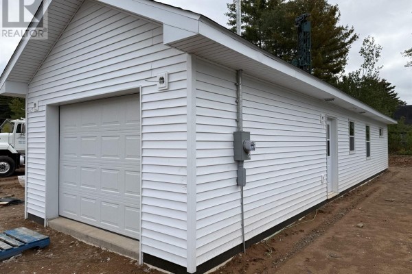 Side view of a white vinyl-sided house showing a garage and electrical meter. - 24 Peterson Street, Cambridge