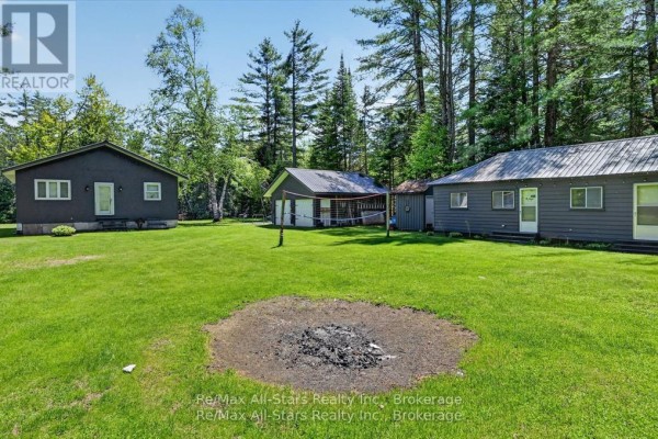 Three detached buildings on a grassy lawn with a fire pit. - 24 Relax Avenue, Kawartha Lakes
