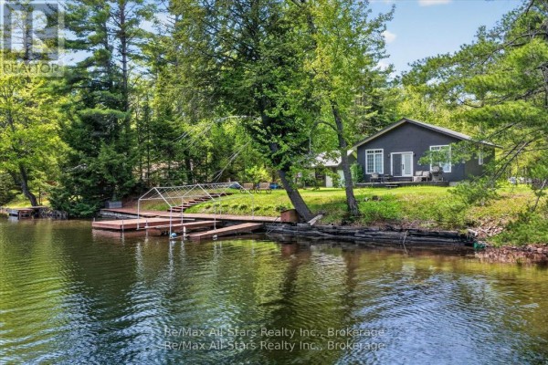 Dark grey bungalow with a wooden dock extending into the water. - 24 Relax Avenue, Kawartha Lakes