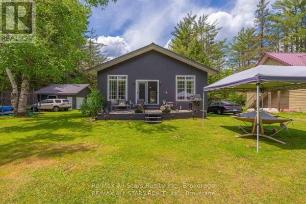 Back of a dark grey bungalow with a deck and a carport. - 24 Relax Avenue, Kawartha Lakes
