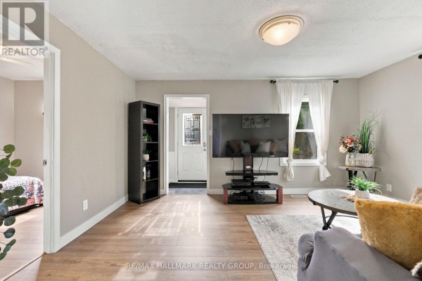 Living room with a large TV, bookshelf, and view into a bedroom. - 24 Reuben Cr Crescent, North Grenville