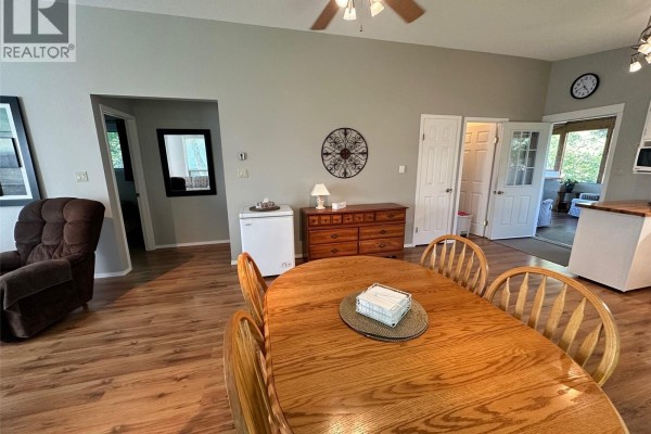 Dining area with wood table and chairs, dresser, mini-fridge, and double doors to an outdoor space. - 24 Ruby Crescent, Hudson Bay Rm No  394