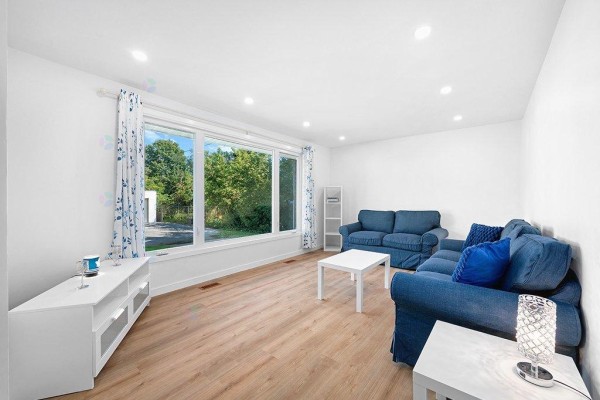 Spacious, white-walled living area with light wood-look flooring and large windows on two walls. - 24 Rue Rear, Pontiac