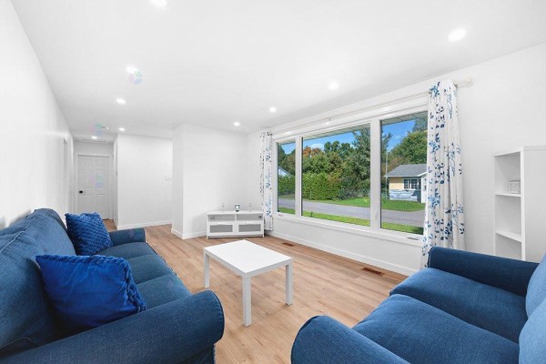 Living room with wide windows showcasing a suburban street and surrounding greenery outside. - 24 Rue Rear, Pontiac