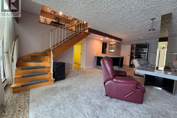 Living room with a wooden staircase, carpeted floors, and a burgundy recliner. - 24 Rue Veteran Sud, Grand Falls