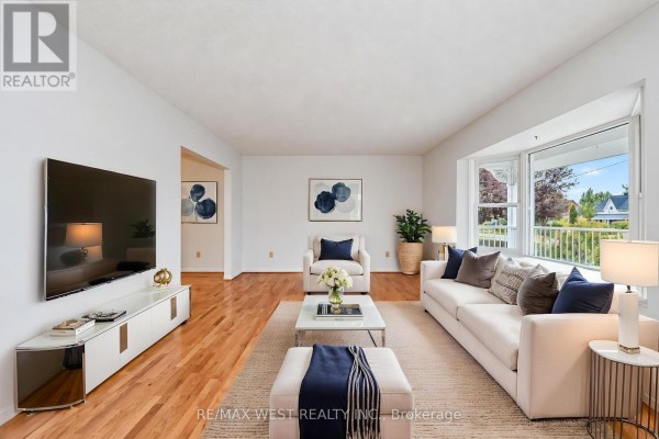 Living room with white walls, hardwood floors, a large white sectional sofa, and a bay window overlooking the yard. - 24 Smith Drive, Uxbridge
