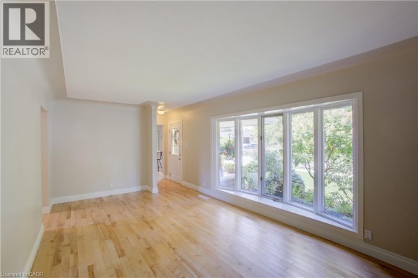 Living room with light wood floors and a large bay window overlooking the garden. - 24 Valewood Place, Kitchener