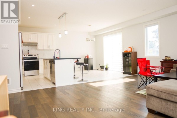 Open-concept living area with a kitchen island, white cabinets, stainless steel appliances, and hardwood floors. - 24 Welch Court, St  Thomas