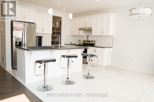 Kitchen area with white cabinetry, stainless steel appliances, a dark countertop island with three stools, and white tile floor. - 24 Welch Court, St  Thomas