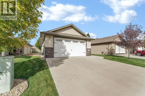 Side view of a beige house with a white garage door and a concrete driveway. - 24 Wheatland Drive Se, Medicine Hat