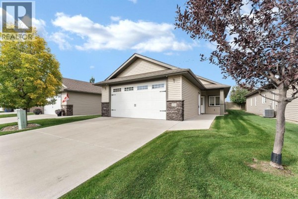 View of a beige house with a double garage door and neat green lawn. - 24 Wheatland Drive Se, Medicine Hat