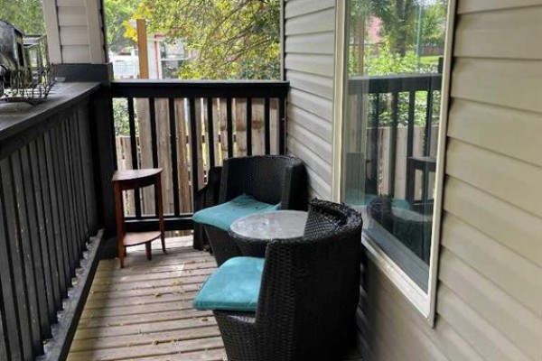Small covered porch with two wicker chairs and a small table with teal cushions. - 240 20 Street N, Lethbridge