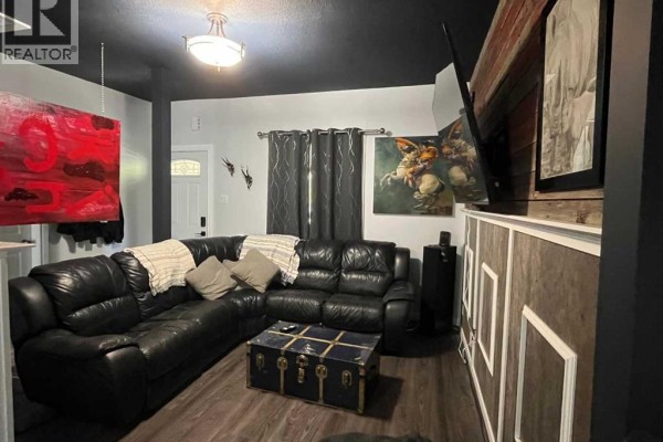 Living room with a large black leather sectional couch, trunk coffee table, and dark walls. - 240 20 Street N, Lethbridge