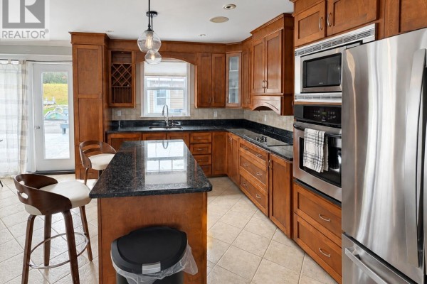 Kitchen with dark granite countertops, cherry wood cabinets, stainless steel appliances, and an island with stools. - 240 Bonds Path, Placentia