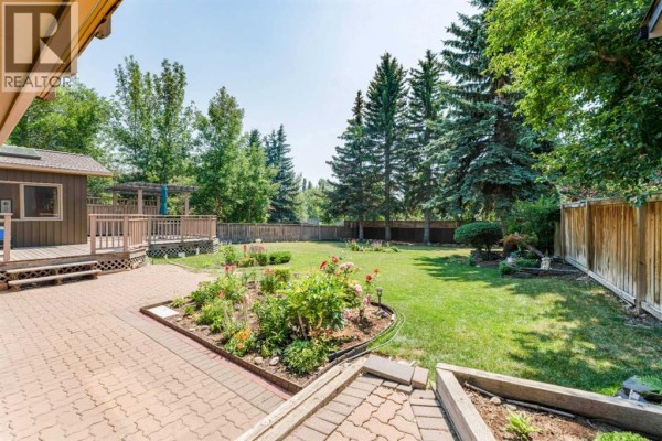 Front view of the house with a covered entryway, large front yard, and mature trees. - 240 Canterville Drive Sw, Calgary