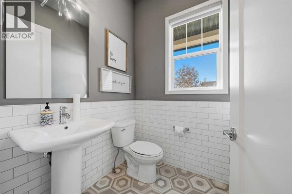 Powder room with a pedestal sink, white subway tile wainscoting, and hexagon floor tiles. - 240 D'arcy Ranch Drive, Okotoks