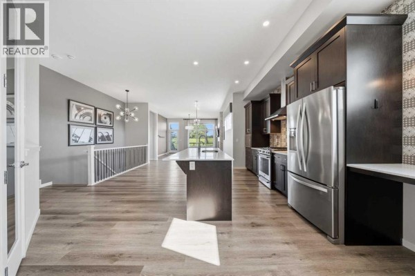 Kitchen with dark wood cabinets, stainless steel appliances, and island with pendant lighting. - 240 D'arcy Ranch Drive, Okotoks