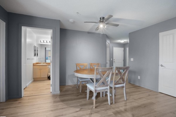 Apartment dining area with wood table, chairs, and view of bathroom with vanity and sinks. - 240 Spruce Ridge Rd, Spruce Grove
