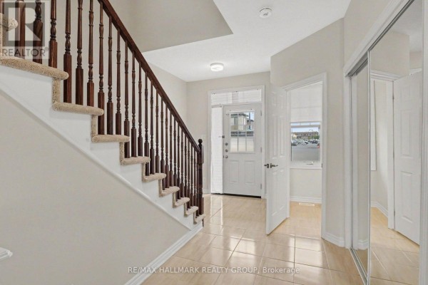 Interior foyer with beige tiled floor, carpeted stairs with wooden railings, and mirrored closet doors. - 240 Sweetvalley Drive, Ottawa