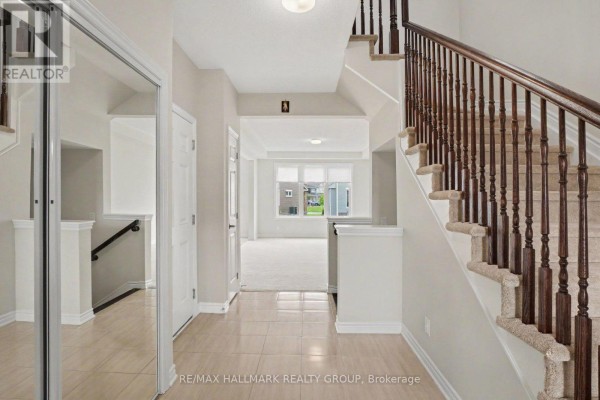 Interior foyer looking towards the living room, featuring beige tiled floor and carpeted stairs with wooden railings. - 240 Sweetvalley Drive, Ottawa