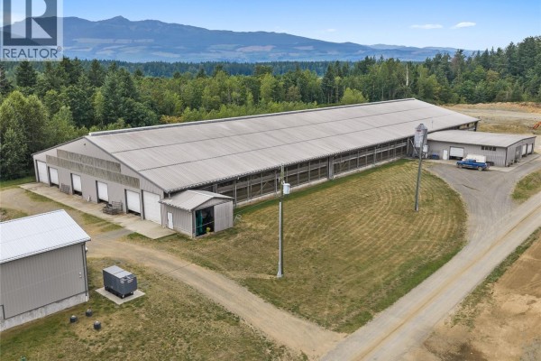 Exterior of a long, silver farm building with multiple garage doors and a small adjacent storage shed. - 2400 Ployart Rd, Black Creek
