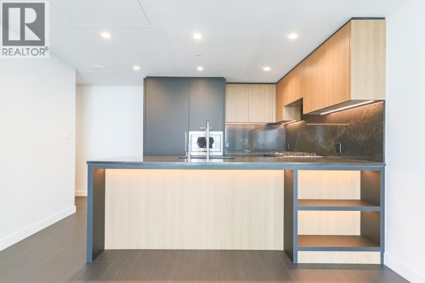 Modern kitchen island with built-in sink, stovetop, and light wood cabinetry. - 2401 6608 Sussex Avenue, Burnaby