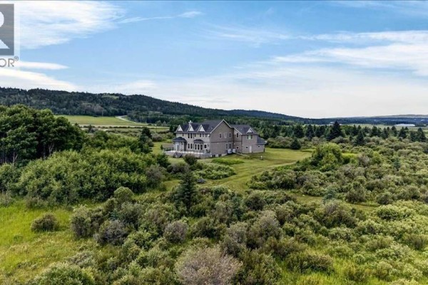 Aerial view of the property showing the house, driveway, and surrounding natural landscape with sparse vegetation. - 240117 210 Avenue W, Rural Foothills County