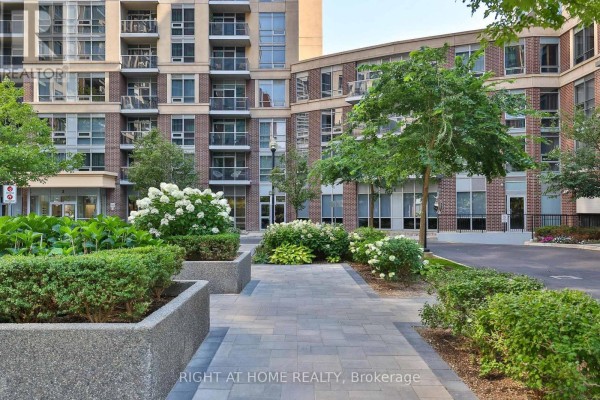A paved walkway leads through a landscaped courtyard with manicured bushes and trees. - 2402 - 3 Michael Power Place, Toronto
