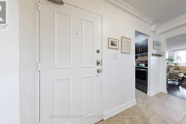 Apartment door and hallway with white doors, beige tiled floor, and a glimpse of the kitchen and living area. - 2402 - 85 Emmett Avenue, Toronto