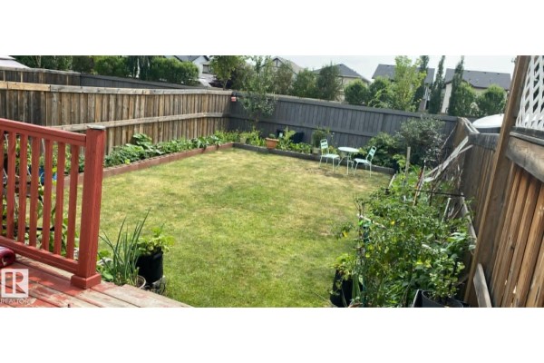 Fully fenced backyard with a green lawn, garden beds, and a small patio set. - 2402 Casselman Cr Sw, Edmonton