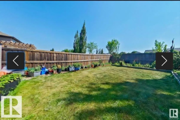 Spacious fenced backyard with a lawn, garden beds, and a wooden fence. - 2402 Casselman Cr Sw, Edmonton