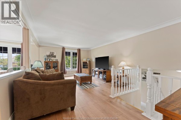 Living room featuring a brown sofa, wood floors, a TV on a media stand, and a white railing. - 2402 St. Alphonse Avenue, Tecumseh