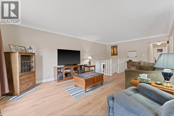 Living room with two sofas, wood floors, a TV, and a view of the staircase leading downstairs. - 2402 St. Alphonse Avenue, Tecumseh