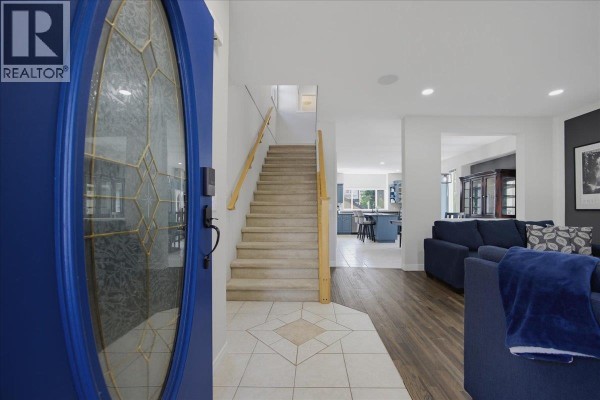 Living room with navy blue sectional sofas, ottoman coffee table, patterned rug, and view of the stairs. - 24030 102a Avenue, Maple Ridge