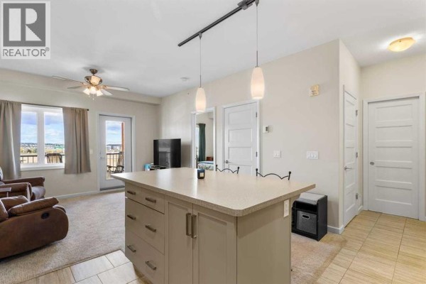 Living and dining area with beige carpet, a recliner chair, and a kitchen island. - 2405, 450 Kincora Glen Road Nw, Calgary