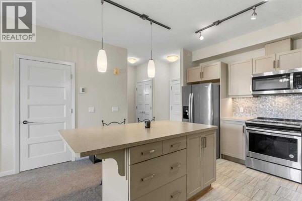Kitchen area with light brown cabinets, stainless steel appliances, and a tiled backsplash. - 2405, 450 Kincora Glen Road Nw, Calgary