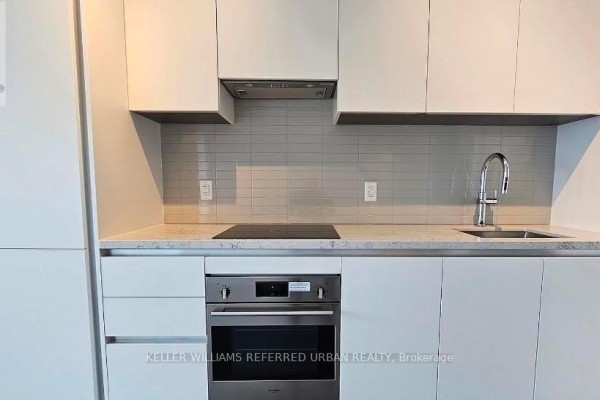 Close-up of a modern kitchen with white cabinetry, a grey tiled backsplash, and stainless steel appliances. - 2405 - 4015 The Exchange Drive, Mississauga