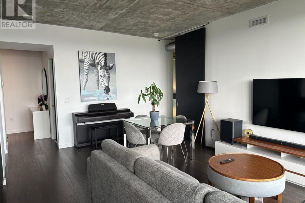Living area with grey sofa, digital piano, glass dining table, and large TV, facing city view. - 2407 - 170 Bayview Avenue, Toronto