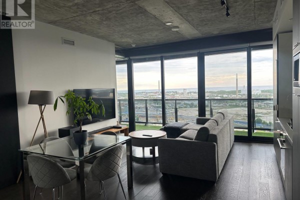 Spacious living room with grey sofa, glass dining table, and large floor-to-ceiling windows overlooking the city. - 2407 - 170 Bayview Avenue, Toronto