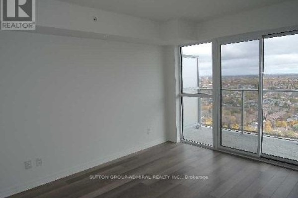 Empty room with floor-to-ceiling windows and glass balcony overlooking a city. - 2407 - 275 Yorkland Road, Toronto