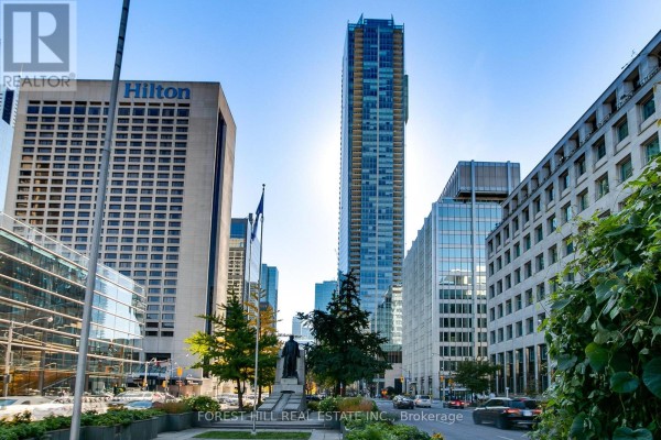 A tall skyscraper stands amidst other buildings and trees on a sunny day. - 2408 - 180 University Avenue, Toronto