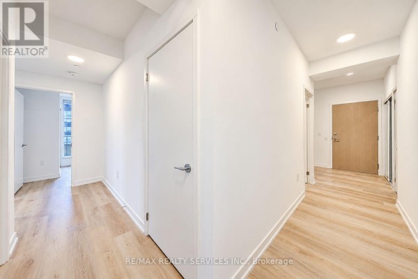 Hallway in an apartment with white walls, light wood floors, and doors to rooms. - 2408 - 395 Square One Drive, Mississauga