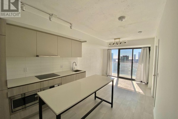 Open concept kitchen and living area with a kitchen island, white countertops, and sliding glass doors. - 2408 - 47 Mutual Street, Toronto