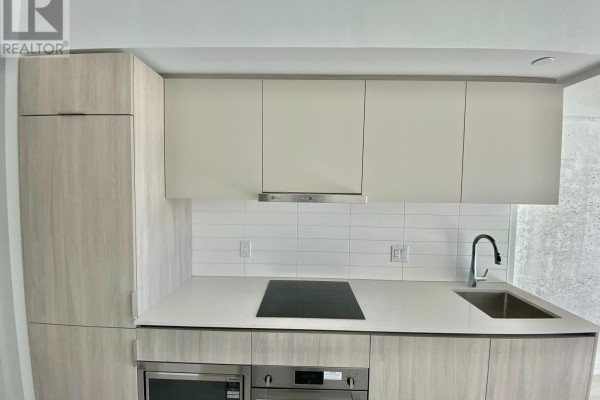 Close-up view of a modern kitchen with light wood cabinets, white tile backsplash, and stainless steel appliances. - 2408 - 47 Mutual Street, Toronto