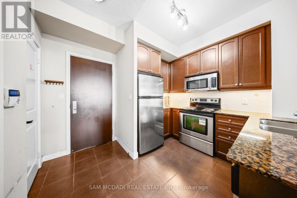 Small kitchen with stainless steel appliances, dark wood cabinets, and granite countertops. - 2408 - 60 Absolute Avenue, Mississauga