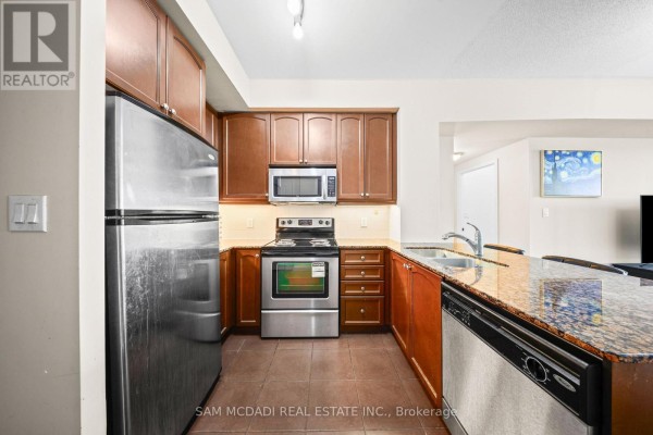 Kitchen with stainless steel refrigerator, stove, microwave, dark wood cabinets, and granite island. - 2408 - 60 Absolute Avenue, Mississauga