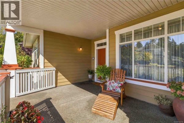 Side exterior view of a tan vinyl-sided house with a lawn and mature trees. - 2409 Poplar Dr, Sooke
