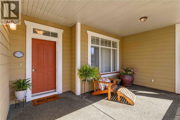 Covered front porch with a wooden chair, ottoman, and potted plants. - 2409 Poplar Dr, Sooke