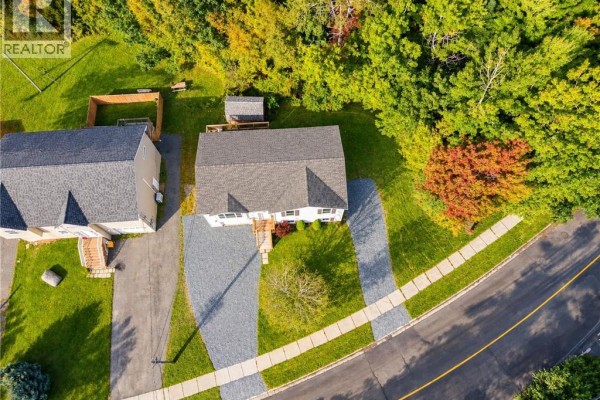 Aerial view of a white house with a grey driveway and surrounding trees. - 241 Claudie Road, Fredericton