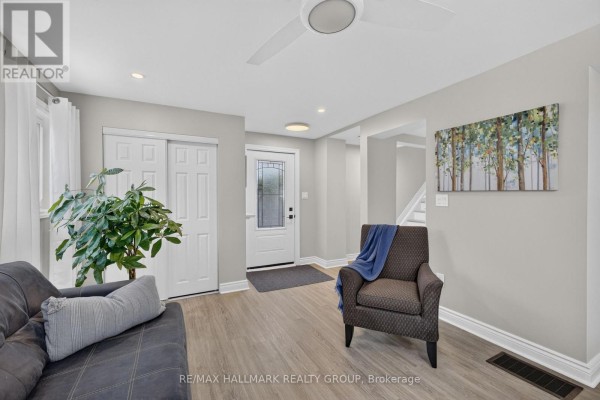 Open concept living area with a sofa, armchair, and view of the front entrance and staircase. - 241 Lewis Street E, Edwardsburgh/cardinal